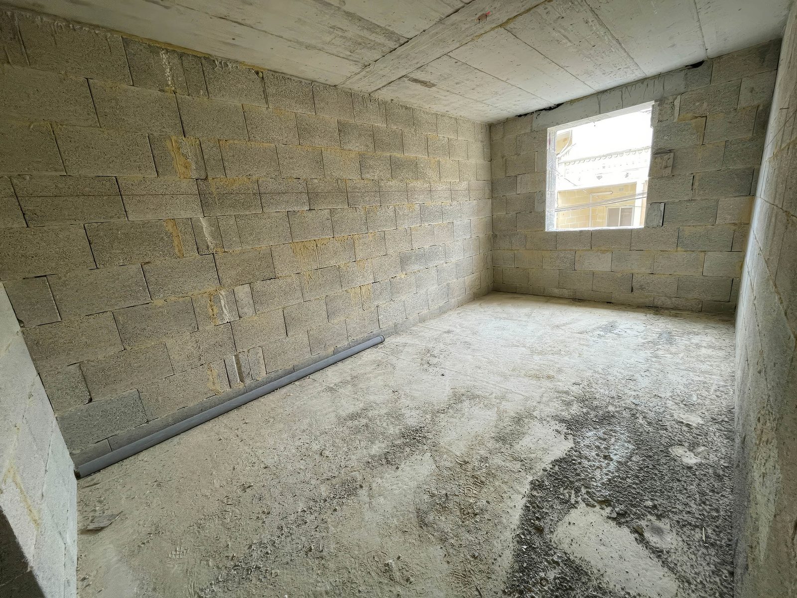 Unfinished apartment: bare limestone block walls, concrete ceiling and a dusty floor